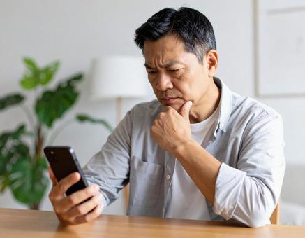 スマートフォンを見ながら思案する男性の写真