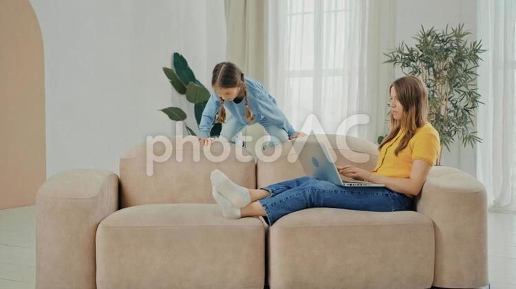 ソファーに座ってテレワークする女性と横で遊ぶ女の子 親子,女の子,娘の写真素材