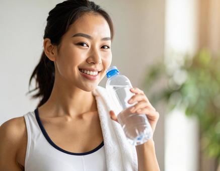 運動後にペットボトルの水を飲む女性 運動後にペットボトルの水を飲む女性の写真