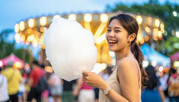 遊園地で綿あめを食べる女性 遊園地で綿あめを食べる女性の写真