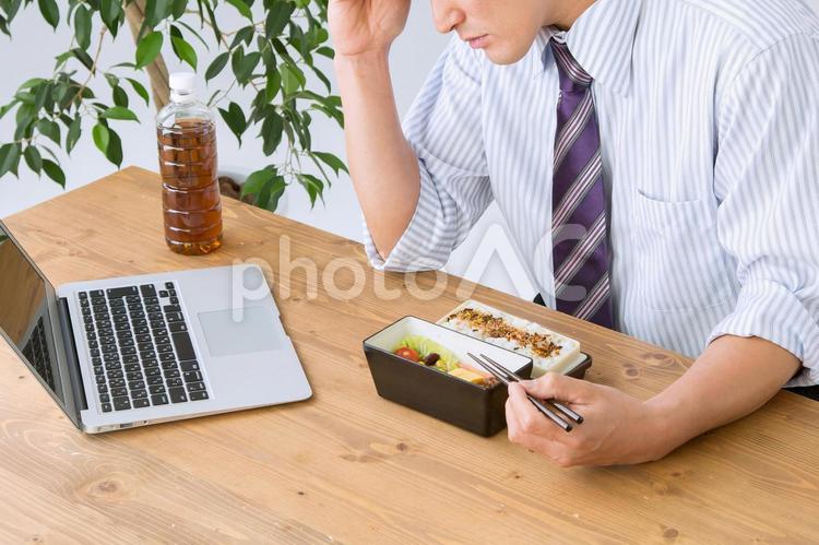 お弁当を食べながら仕事する男性（頭痛） 食欲不振,体調不良,ストレスの写真素材