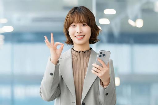 スマホを持ってOKポーズをする笑顔の女性 女性,ok,スマホの写真素材