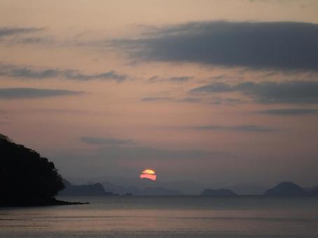 海と山の向こうに沈む夕日の写真