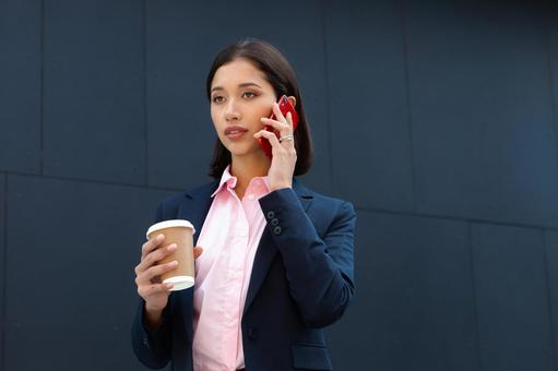 オフィスビルの外でコーヒー片手に電話する女性 ビジネスウーマン,ビジネス,女性の写真素材