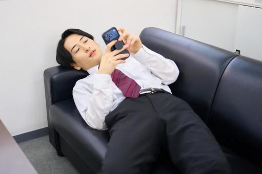 ソファに寝転んでスマホを見るビジネスマン ビジネスマン,スマホ,ソファの写真素材