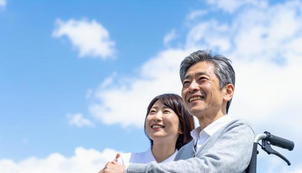 青空を見つめる車いすシニアと介護の女性の写真