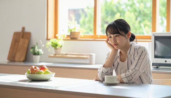 疲れた表情でキッチンに座る若い女性 疲れた表情でキッチンに座る若い女性の写真