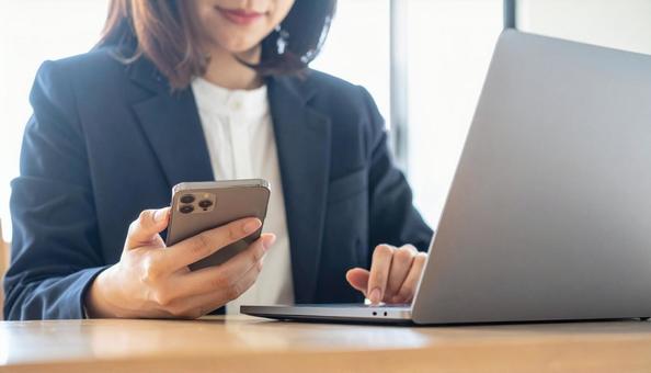 携帯を操作する女性の手元とノートパソコンの写真