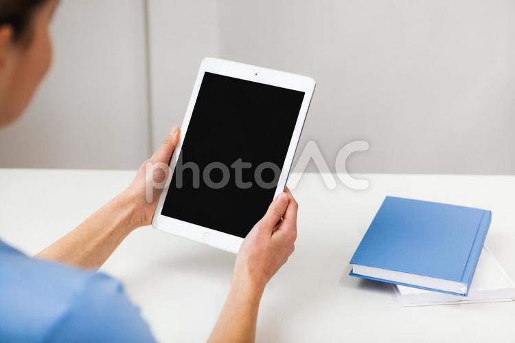 両手で持つタブレットと横に置かれた本 タブレット,画面,持つの写真素材