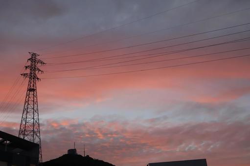 茜色の夕空と鉄塔とシルエットの建物と山 茜色の夕空と鉄塔とシルエットの建物と山の写真