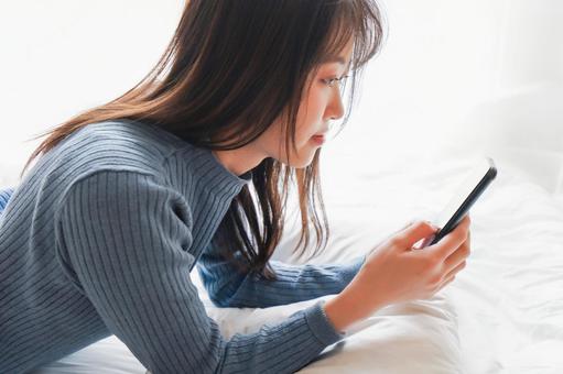 ベッドで寝る前にスマホを使う若い女性 ベッドで寝る前にスマホを使う若い女性 視力低下,マンガ,女性の写真素材
