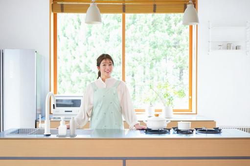 キッチンに立つ笑顔のエプロン女性 キッチンに立つ笑顔のエプロン女性の写真