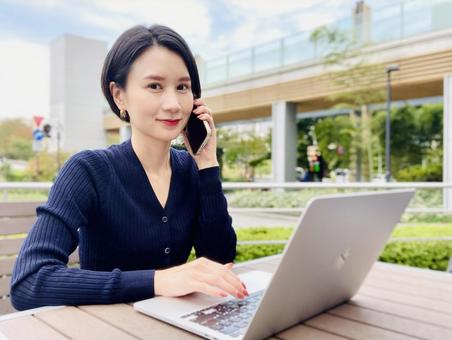 Smiling woman doing remote work in the park, computer, mobile phone, smartphone, JPG