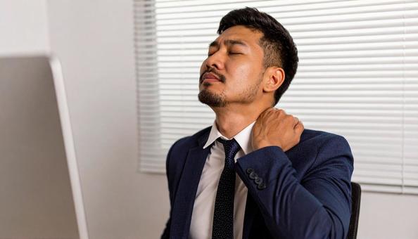 デスクワークで肩を回しほぐすビジネスマンの写真