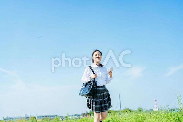 青空の下を歩く女子高校生 スマホ,高校生,笑顔の写真素材