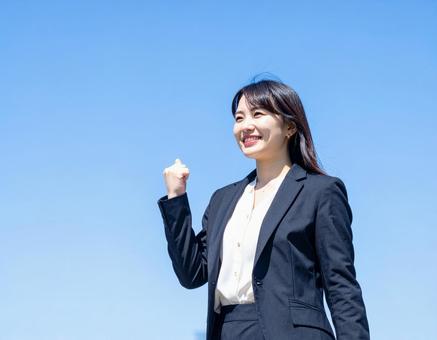 青空の下ガッツポーズする女性社員 青空の下ガッツポーズする女性社員の写真