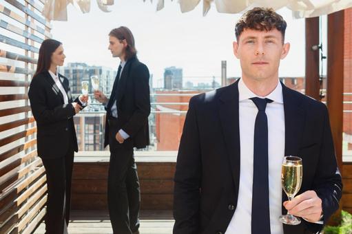 会話中の男女の前でカメラ目線の外国人男性 男性,シャンパングラス,持つの写真素材