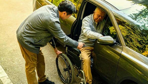 車椅子高齢男性の車の乗車を介助する男性 車椅子高齢男性の車の乗車を介助する男性の写真