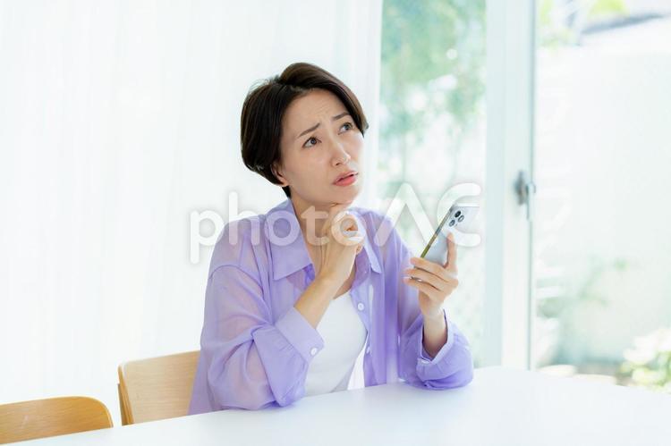 スマホを持って考える女性 スマホ,考える,悩むの写真素材