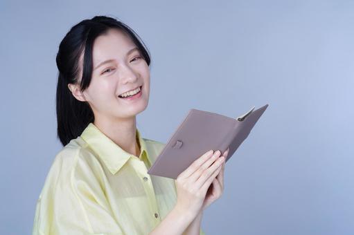 手帳を見て微笑む黄色い服の女性 女性,手帳,持つの写真素材