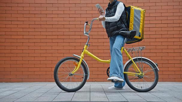 自転車にまたがったままスマートフォンを使うフードデリバリーの女性 配達,フードデリバリー,デリバリーの写真素材