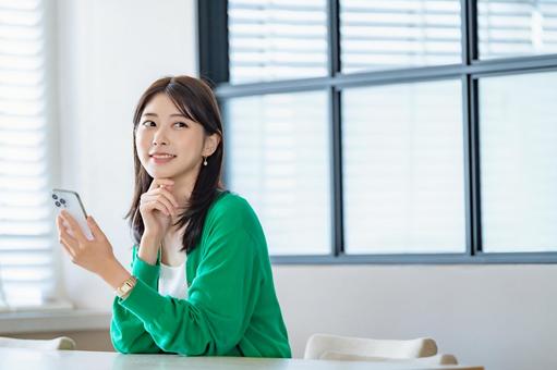 室内でスマートフォンを持ち微笑む女性 室内でスマートフォンを持ち微笑む女性 女性,スマートフォン,携帯電話の写真素材