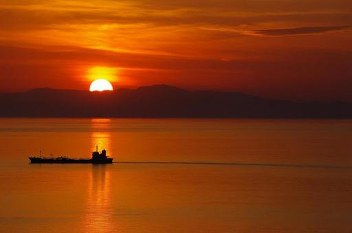 夕焼けの海を進む小舟と水平線に沈む太陽 夕焼けの海を進む小舟と水平線に沈む太陽の写真