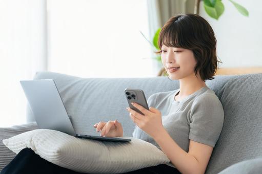 ソファに座ってスマホとパソコンを使う女性 ソファに座ってスマホとパソコンを使う女性 女性,ソファ,パソコンの写真素材