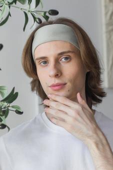 顎を触るヘアバンドをしたカメラ目線の男性の写真