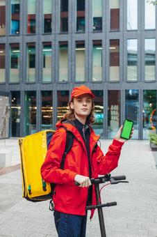 街なかでスマートフォンの画面を見せているフードデリバリーの男性 配達,フードデリバリー,デリバリーの写真素材