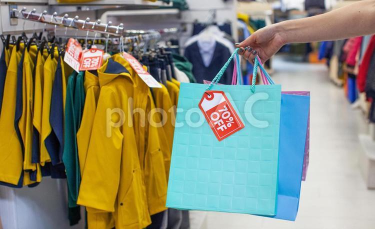 洋服売り場でセールのタグの付いた紙袋を持っている女性の手 セール,ショップ,女性の写真素材