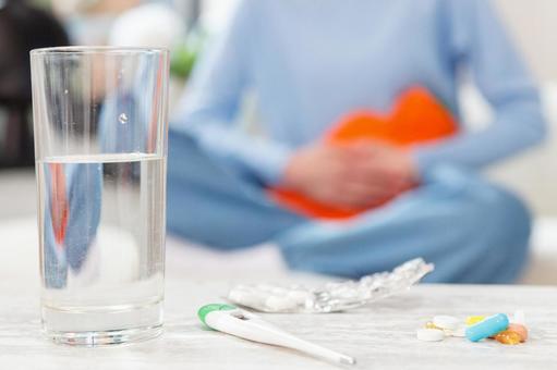 グラスの水と錠剤と体温計と生理痛でお腹を温める女性 生理,月経,女性の写真素材