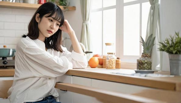 疲れた表情でキッチンに座る若い女性 疲れた表情でキッチンに座る若い女性の写真