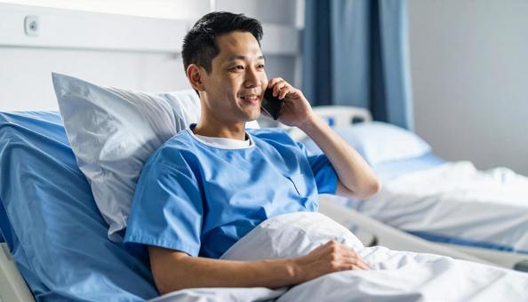 病室のベッドから携帯で話をする男性患者 病室のベッドから携帯で話をする男性患者の写真