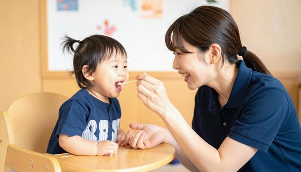 子どもにご飯をあげる保育士の写真