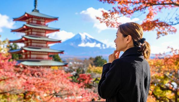 紅葉する木の下で顎に手をやり考える女性の写真