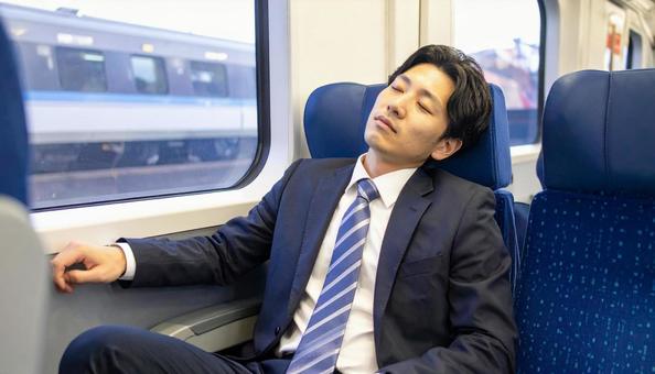 電車で仮眠をする会社員の男性 電車で仮眠をする会社員の男性の写真