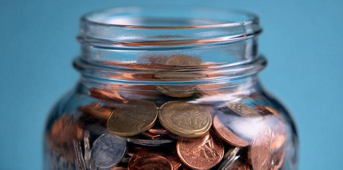 青い背景に輝く、コインが詰まった貯金瓶 青い背景に輝く、コインが詰まった貯金瓶の写真