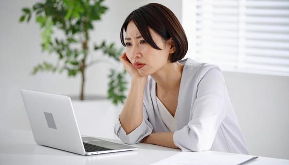 パソコンの前で考える女性社員 パソコンの前で考える女性社員の写真