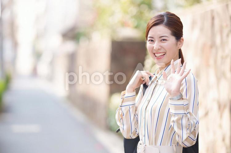 笑顔で振り向いて手を振る女性の上半身 女性,カメラ目線,にっこりの写真素材