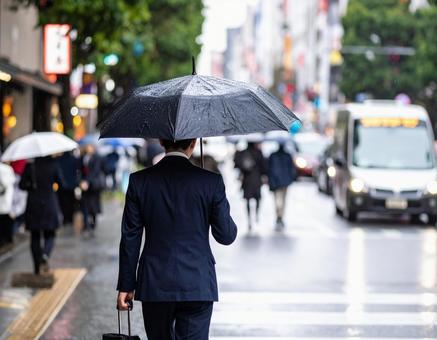 梅雨時、傘をさして街中を歩くビジネスマン 梅雨時、傘をさして街中を歩くビジネスマンの写真