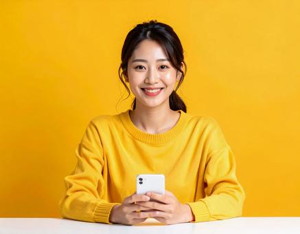 スマホを持つ笑顔の女性 黄色背景 スマホを持つ笑顔の女性 黄色背景の写真
