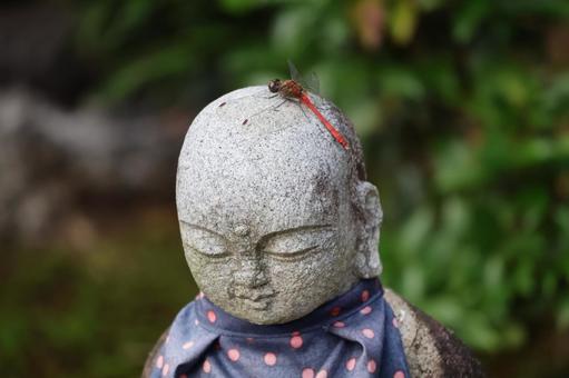 お地蔵様の頭にとまる赤とんぼの写真