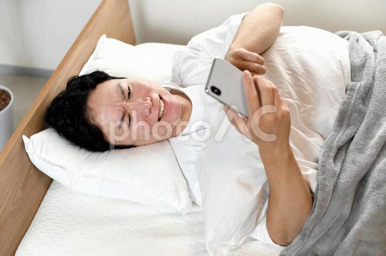 ベッドの上でスマホを持ちながら困る男性 男性,スマホ,寝室の写真素材