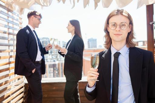 カメラ目線でシャンパンを持つ男性と後ろで話している男女 男性,外国人,シャンパングラスの写真素材