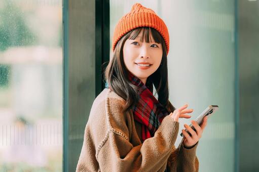 冬の街角でスマホを使う笑顔の女性 冬,女性,街の写真素材
