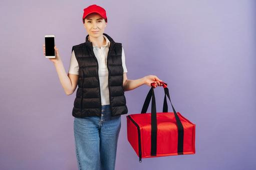 保温ピザバッグを持つってスマートフォンの画面を見せる女性配達員 配達,フードデリバリー,デリバリーの写真素材