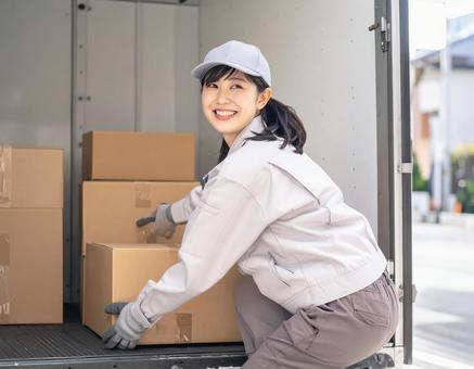 トラックから荷物を出す宅配女性ドライバーの写真