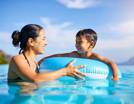 プールで浮き輪に乗る子供を見守る親の写真