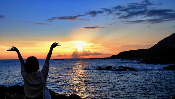 夕陽を見ながら女性がピースしている写真 夕日,人物,後ろ姿の写真素材
